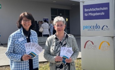 Zwei Frauen mit Flyern der EUTB vor dem Eingang einer Pflegeschule